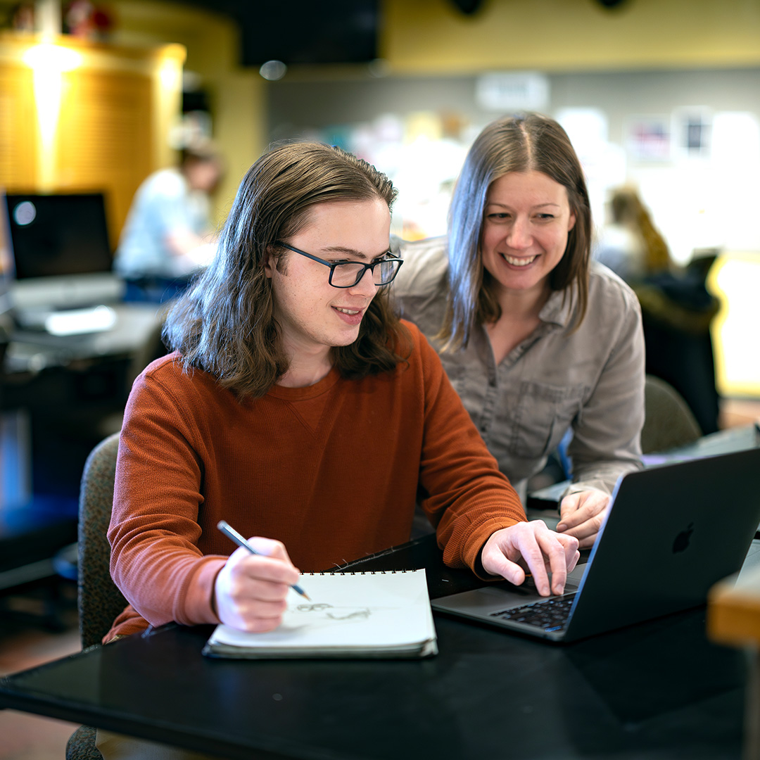 Communication Design Instructor Andrea White helping a student working on a laptop