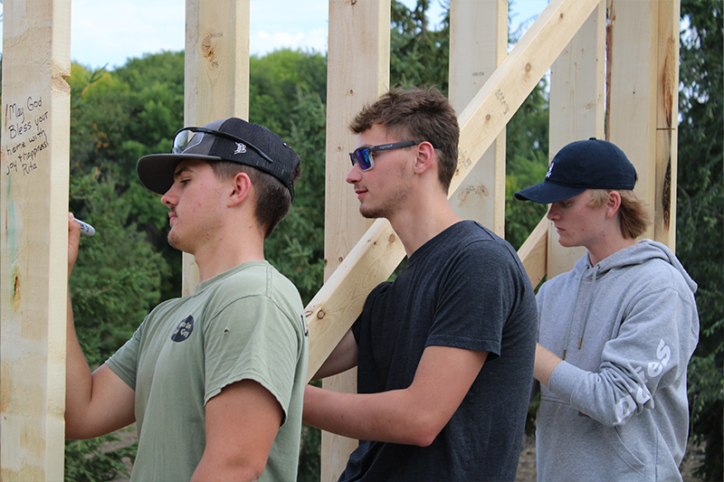 ATCC Carpentry students Nicholas Mielke, Zach Dufault, and Grant Bongard sign messages on to the home owners of the Legends Build project home during the blessing ceremony with volunteers from Habitat for Humanity of Douglas County .