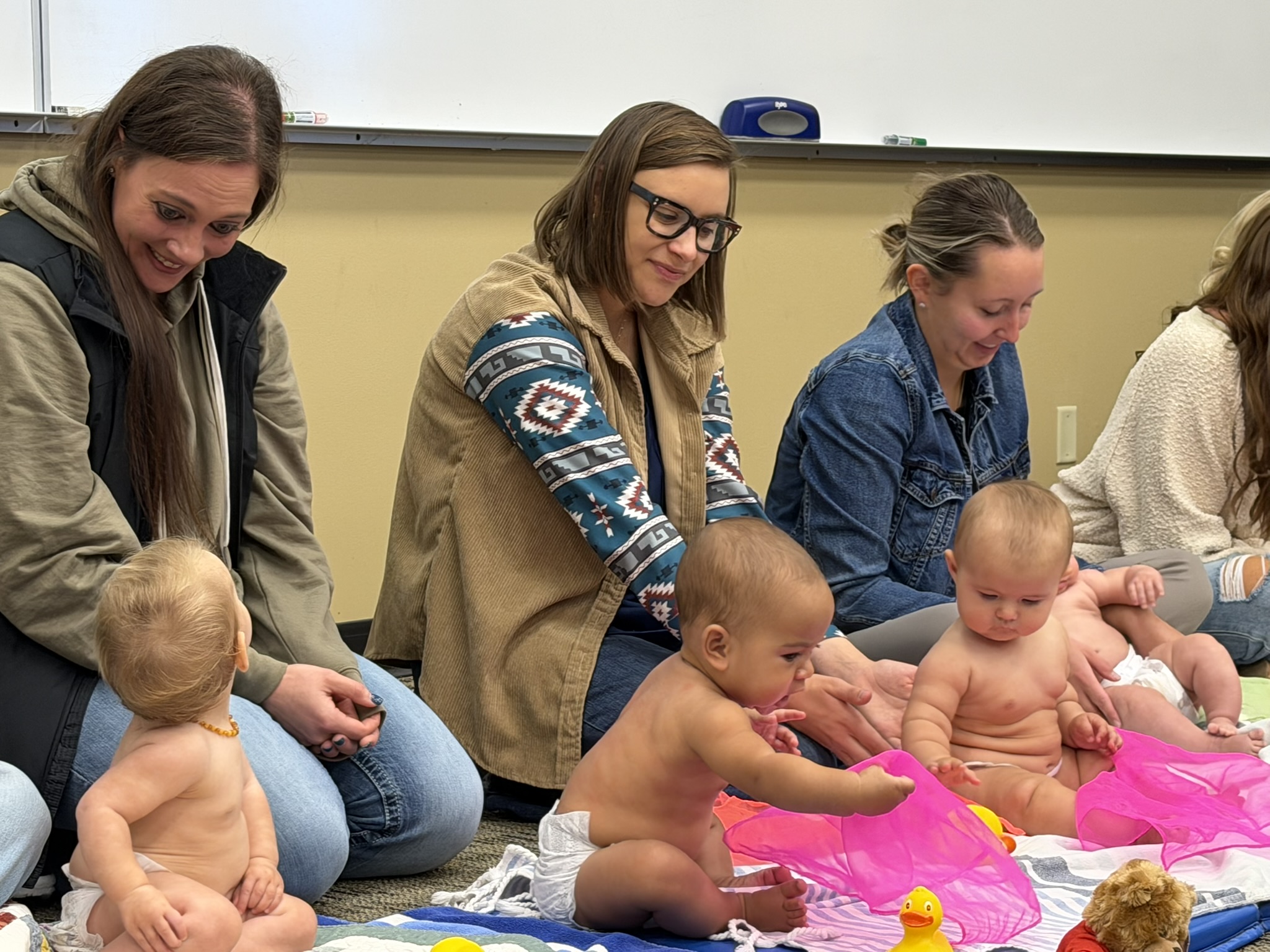 Women and infants seated on a classroom floor