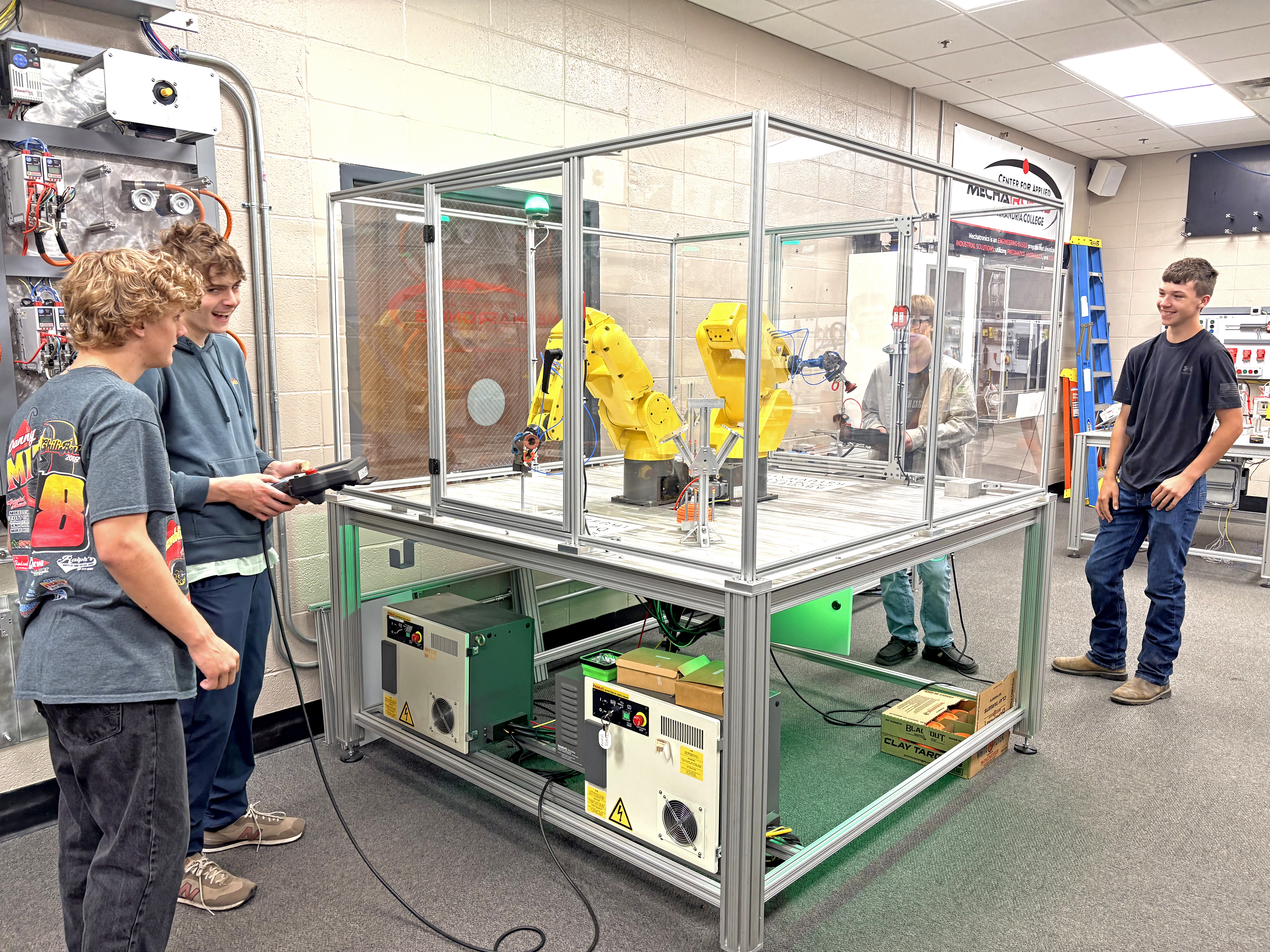 A camp participants holds a remote control device while three other participants watch him operate a mechanical arm