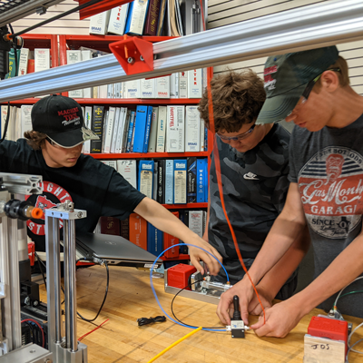 Three students work on an assembly in the Mechatronics classroom