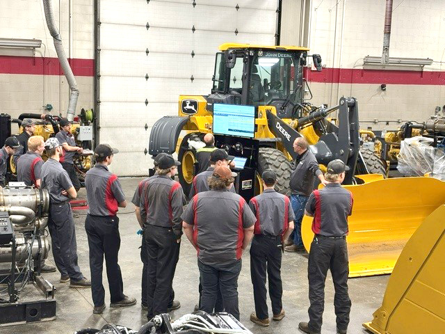 Students stand in a shop next to a large piece of machinery