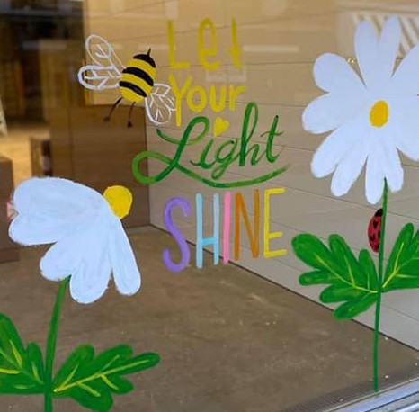 Painting on window of flowers and bees with text "Let your light shine"